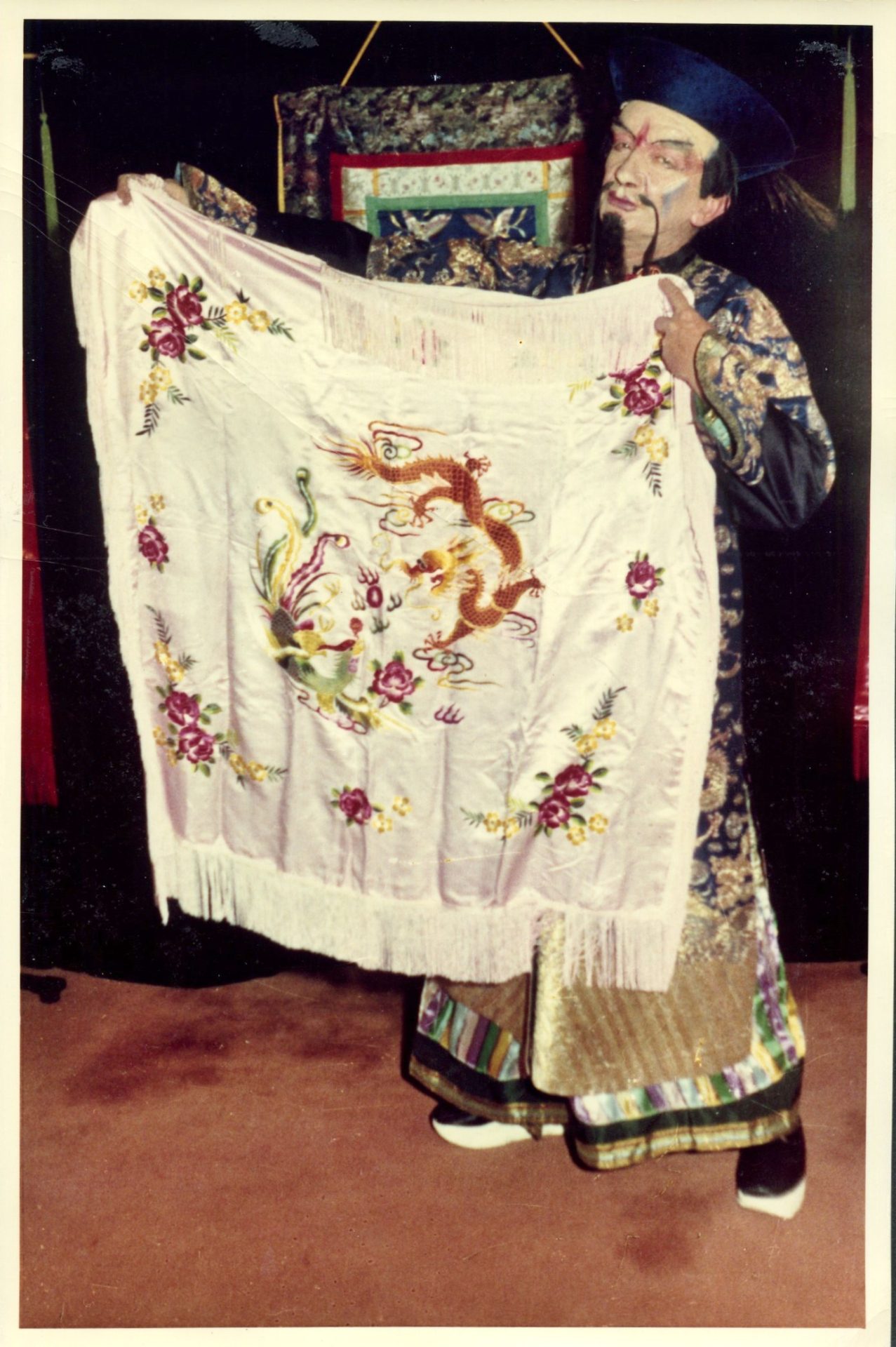 Norman Hunter as Ho Wat Fun  displaying an embroidered cloth